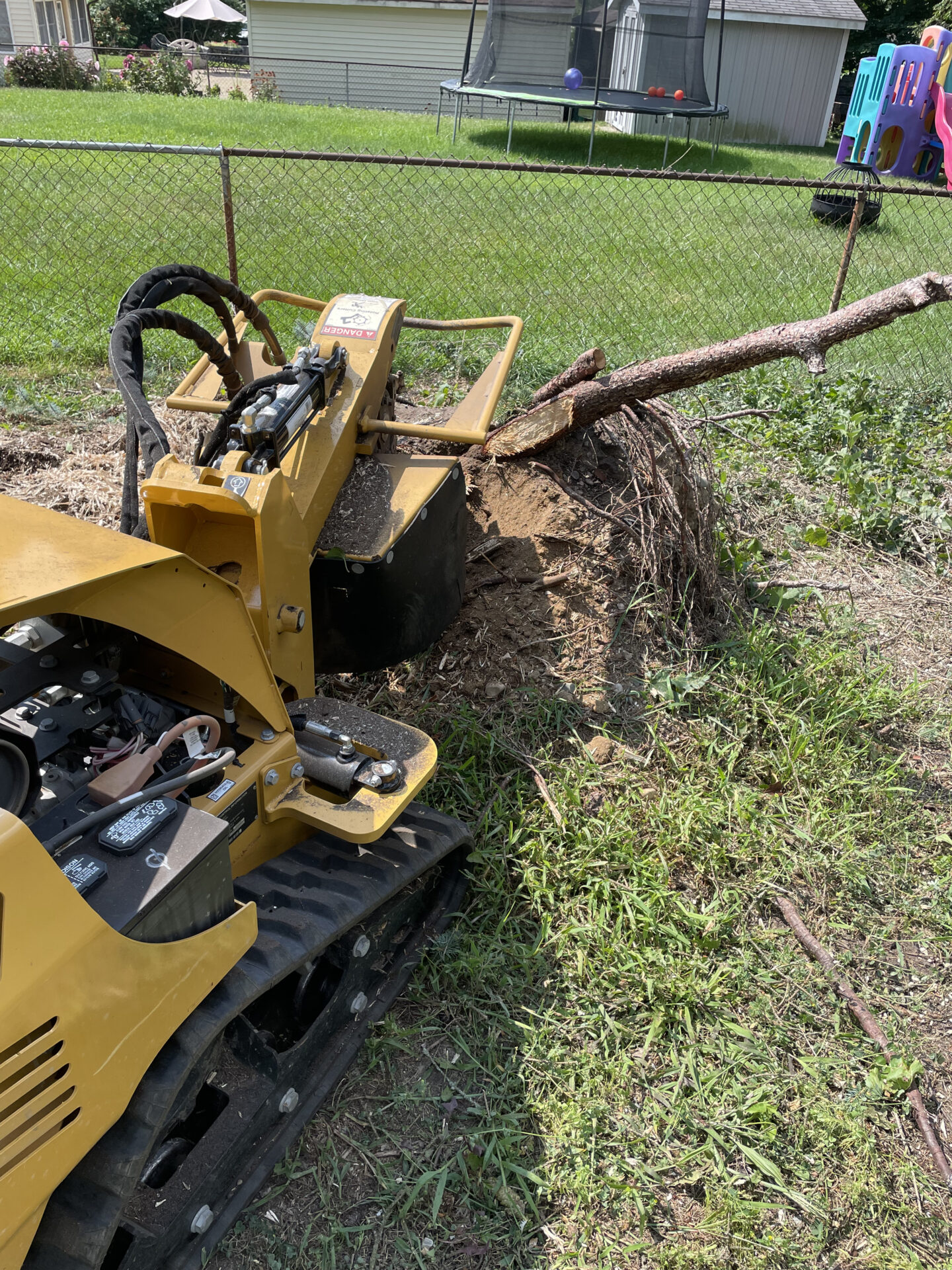 Stump grinder machine removing a tree stump in a residential backyard as part of professional stump grinding service.