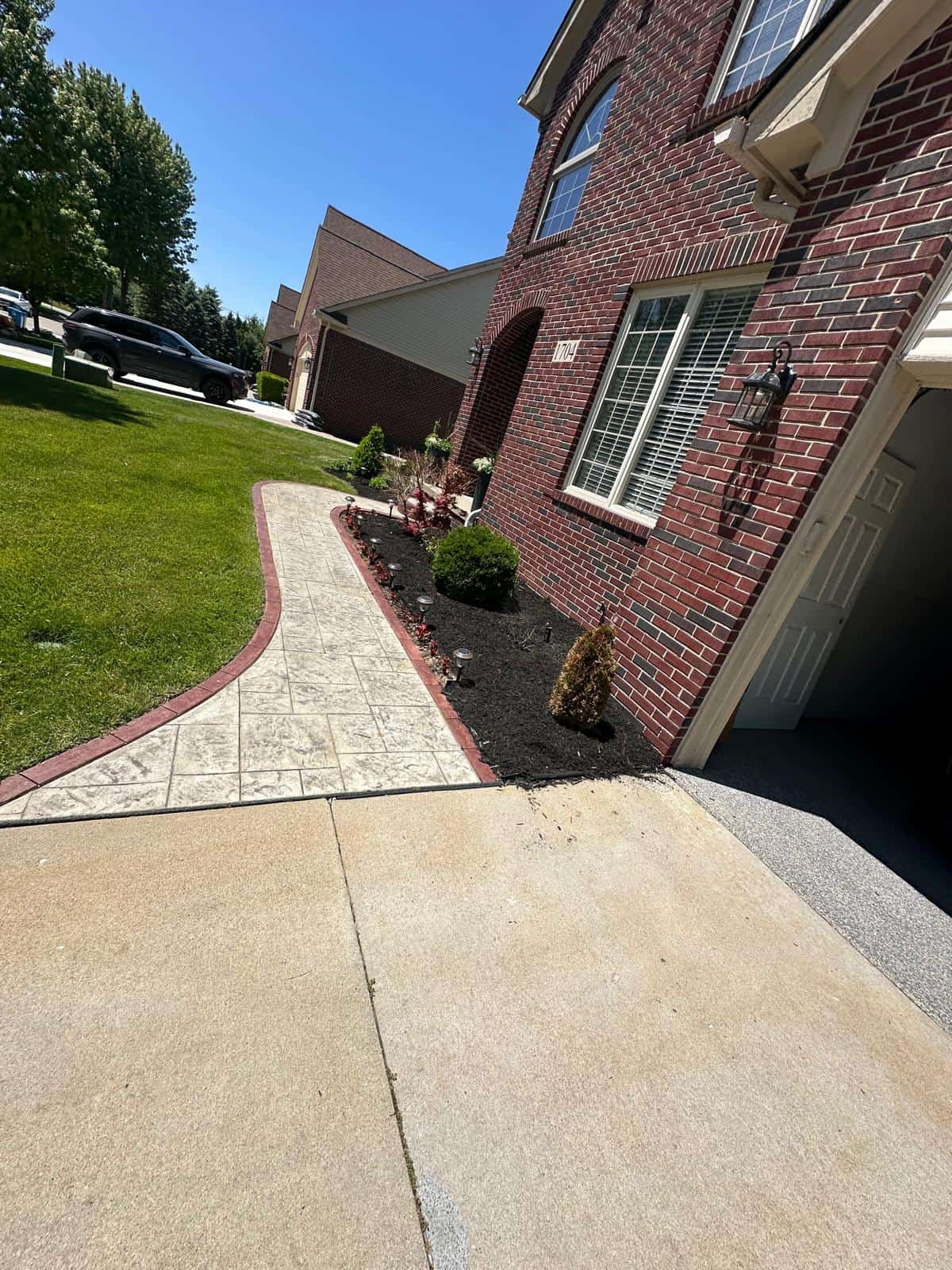A brick house with a lush garden and curved sidewalk, maintained by Tree Services Oakland for curb appeal.