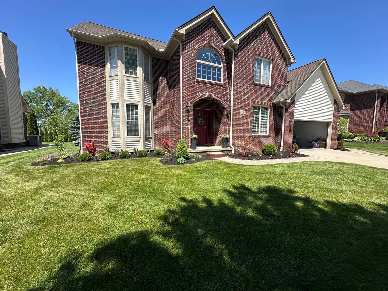 Two-story brick house with manicured lawn, fresh landscaping, and tree removal Oakland services visible.