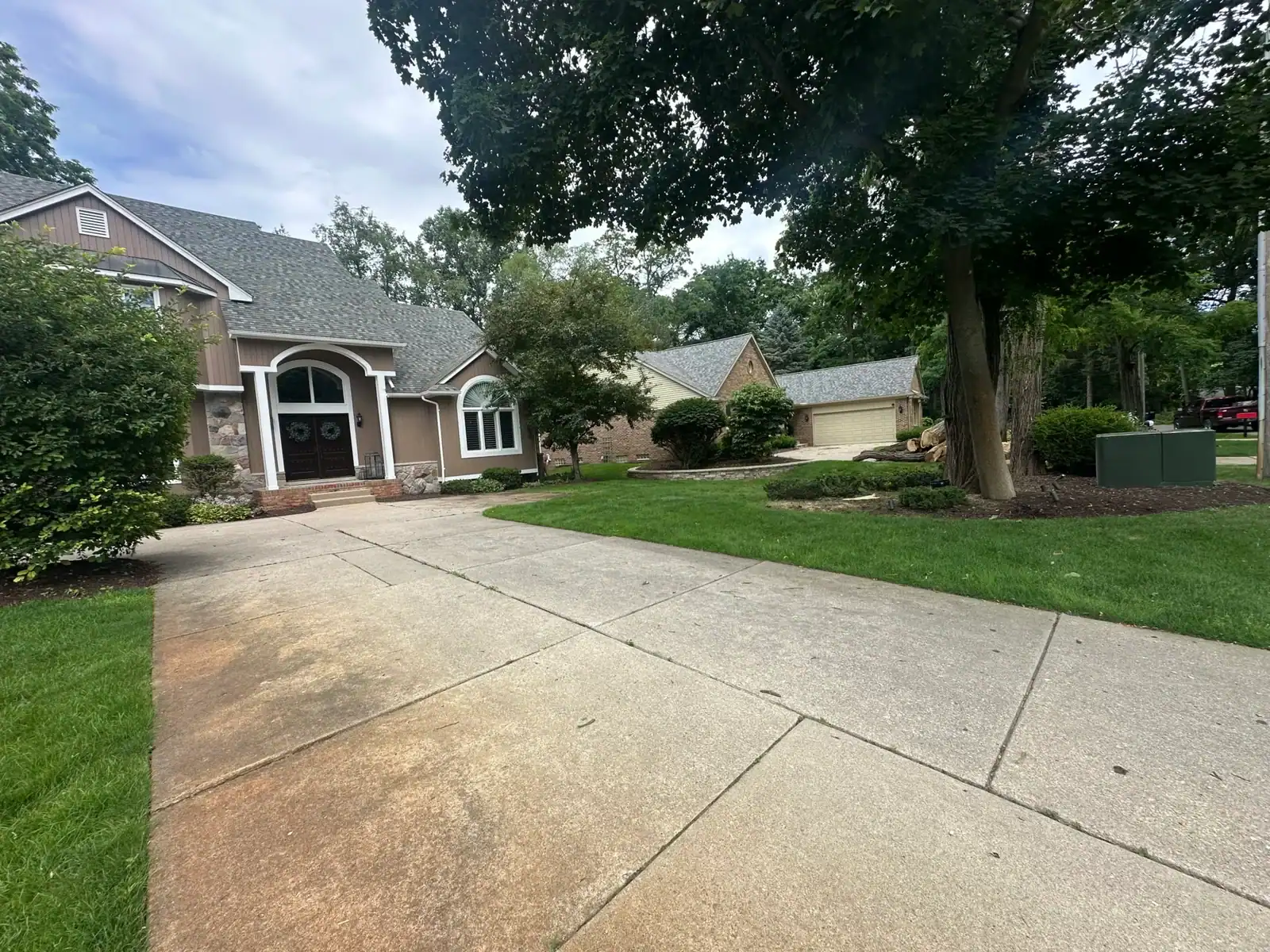 A concrete driveway leads to a Michigan home with trees, grass, and bushes in Oakland.