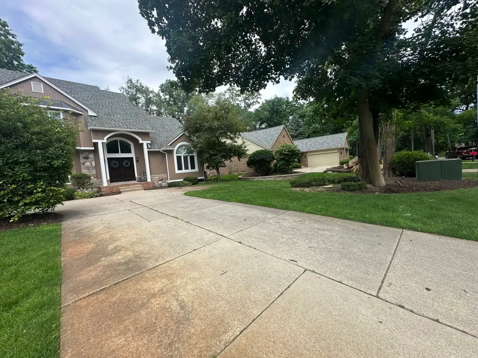 A suburban Oakland house with green lawn and trees highlights Tree Services Oakland, MI nearby.