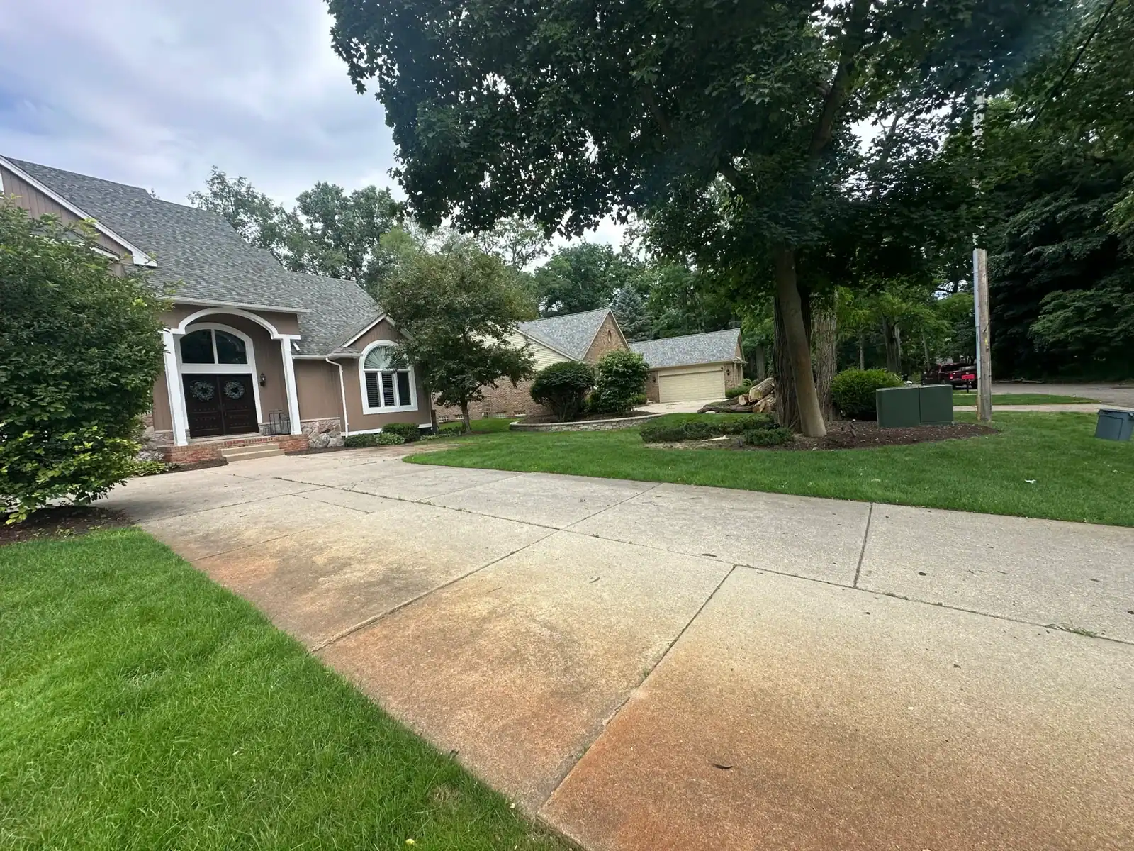Concrete driveway bordered by grass, with Tree Services Oakland maintaining nearby trees and bushes.