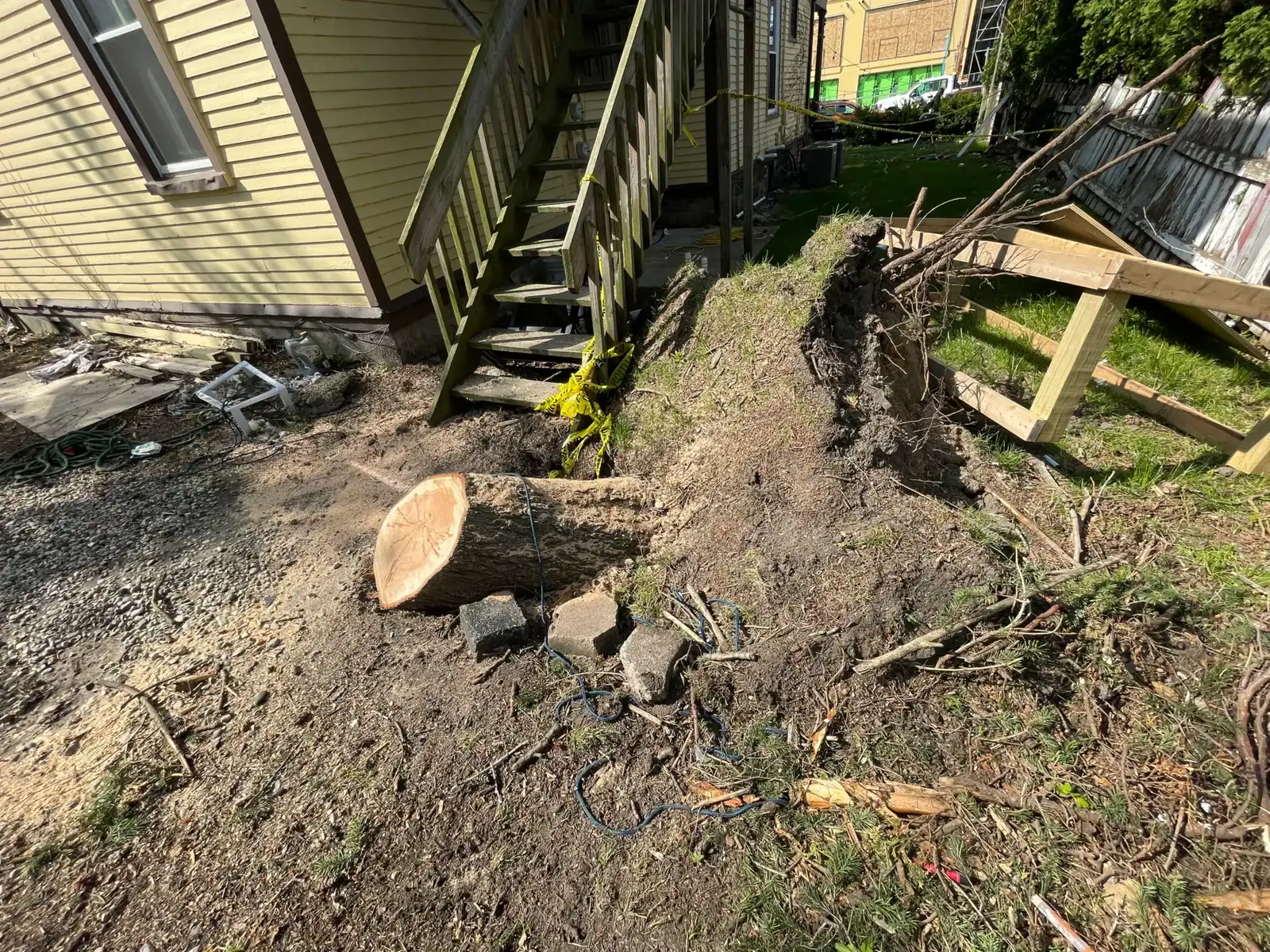 Tree removal Oakland resulted in a fallen tree with exposed roots and cut trunk by house stairs.
