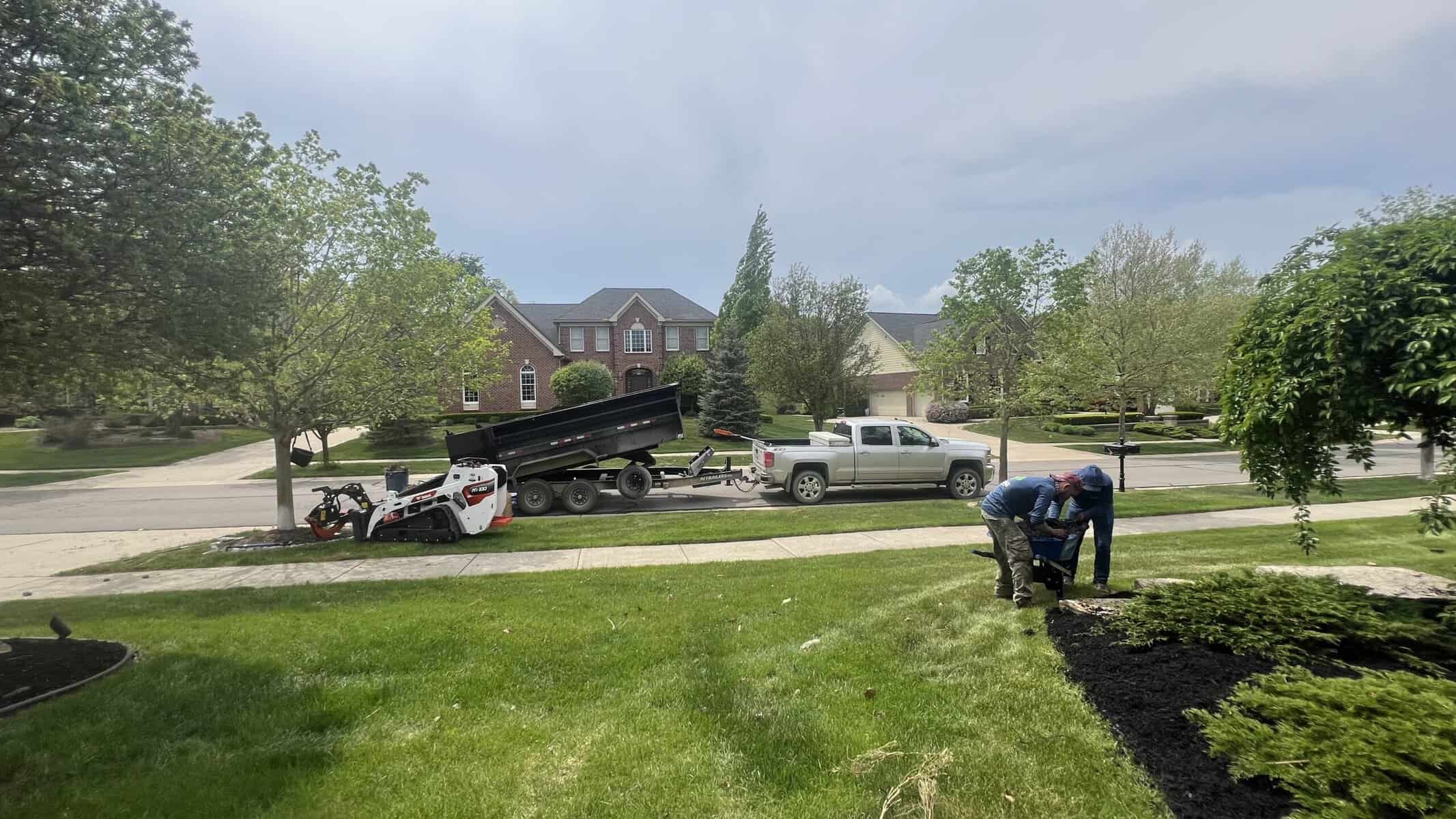 A worker in a blue shirt landscapes a yard with MI tree removal and stump grinding equipment nearby.