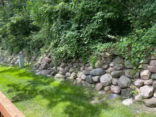 Large rocks form a short retaining wall, bordered by green grass and dense leafy trees in the background.